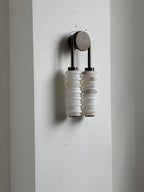 Clérachic sconce unlit on a white wall panel, the two alabaster columns hanging beneath a small bronze arch.
