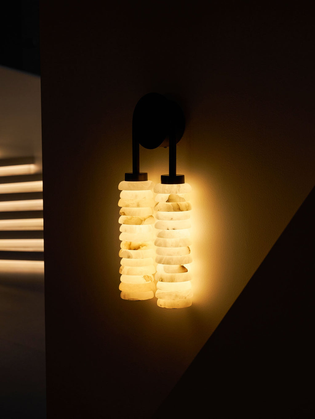 Clérachic sconce glowing bright warm white in a dark room, the veined alabaster discs lit from within.