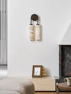 Unlit Clérachic sconce with a dark round backplate on a white wall, above a pale stone ledge, a picture frame and a stone sofa.