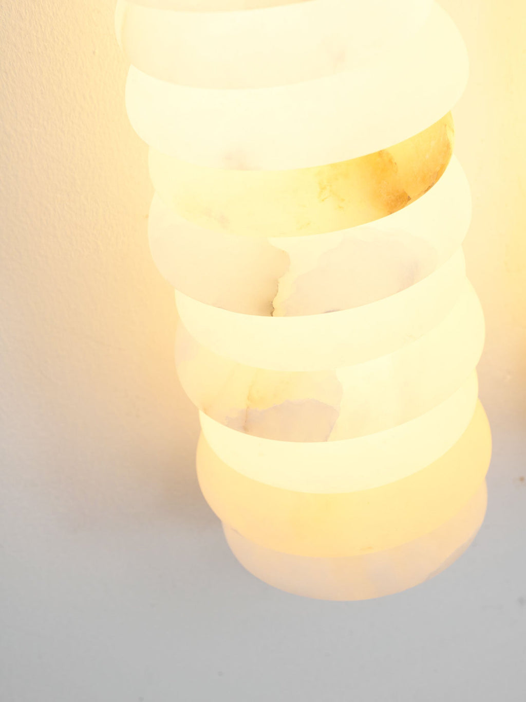 Close view of a lit alabaster column on a Clérachic sconce, the stone rings glowing a warm yellow-white.