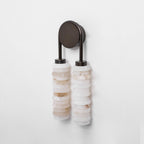 Clérachic sconce unlit on a pale wall, two columns of mixed cream and white alabaster under a dark bronze arch.