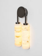 Lit Clérachic sconce in dark bronze on a pale wall, the cream and white alabaster discs glowing a warm yellow.