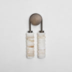 Clérachic sconce unlit on a pale grey wall, an antique-brass arch and plate above two columns of veined cream alabaster.
