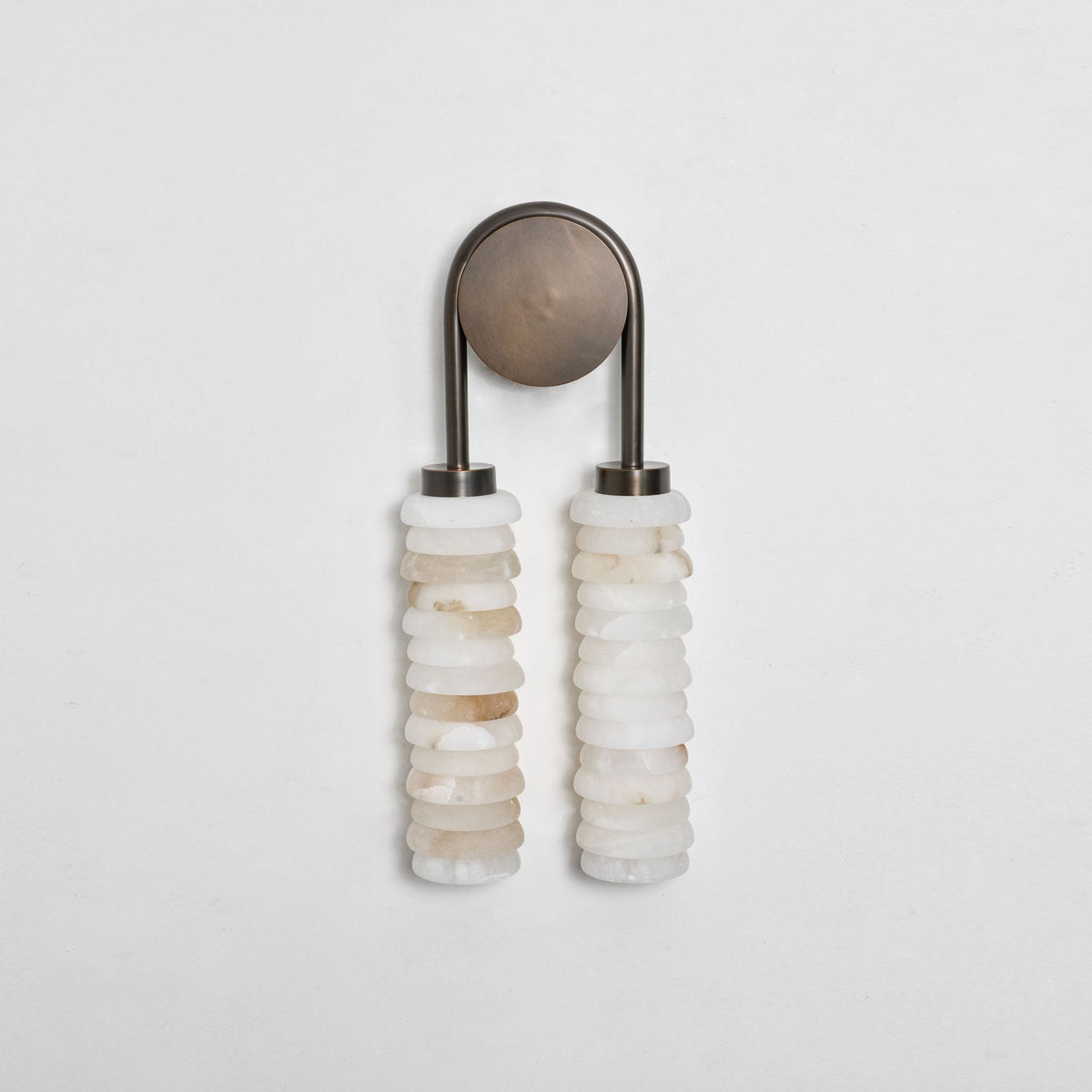 Clérachic sconce unlit on a pale grey wall, an antique-brass arch and plate above two columns of veined cream alabaster.
