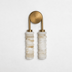 Clérachic sconce with a brushed antique-brass arch and plate, unlit, over two columns of cream alabaster on a pale wall.