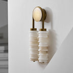 Angled view of a Clérachic sconce in antique brass on a white wall, with white alabaster discs and a pale round backplate.