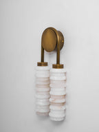 Clérachic sconce with an antique-brass arch and plate seen from the side, over two white alabaster columns on a pale wall.