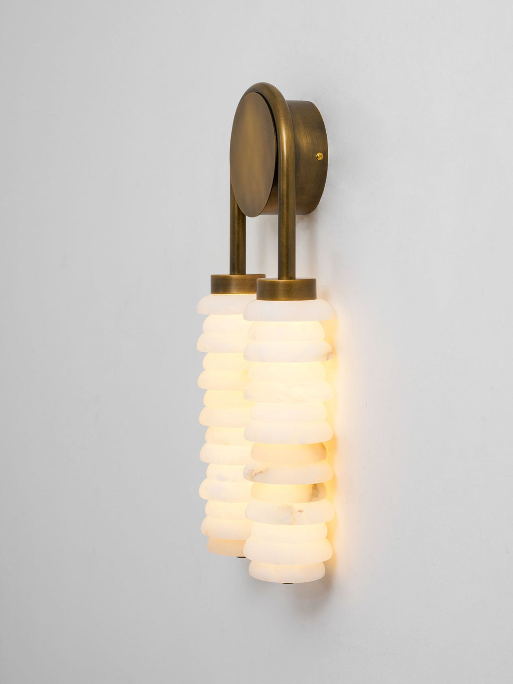 Angled view of a lit Clérachic sconce in antique brass, the alabaster columns glowing white and slightly staggered.
