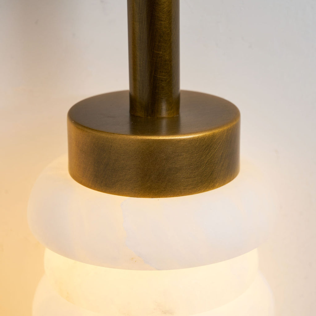 Close view of the antique-brass cap and neck above a glowing alabaster disc on this Clérachic sconce.