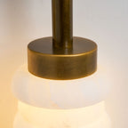 Close view of the antique-brass cap and neck above a glowing alabaster disc on this Clérachic sconce.