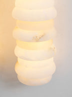 Close view of a lit alabaster column on a Clérachic sconce, the rounded discs glowing with a soft golden-white light.