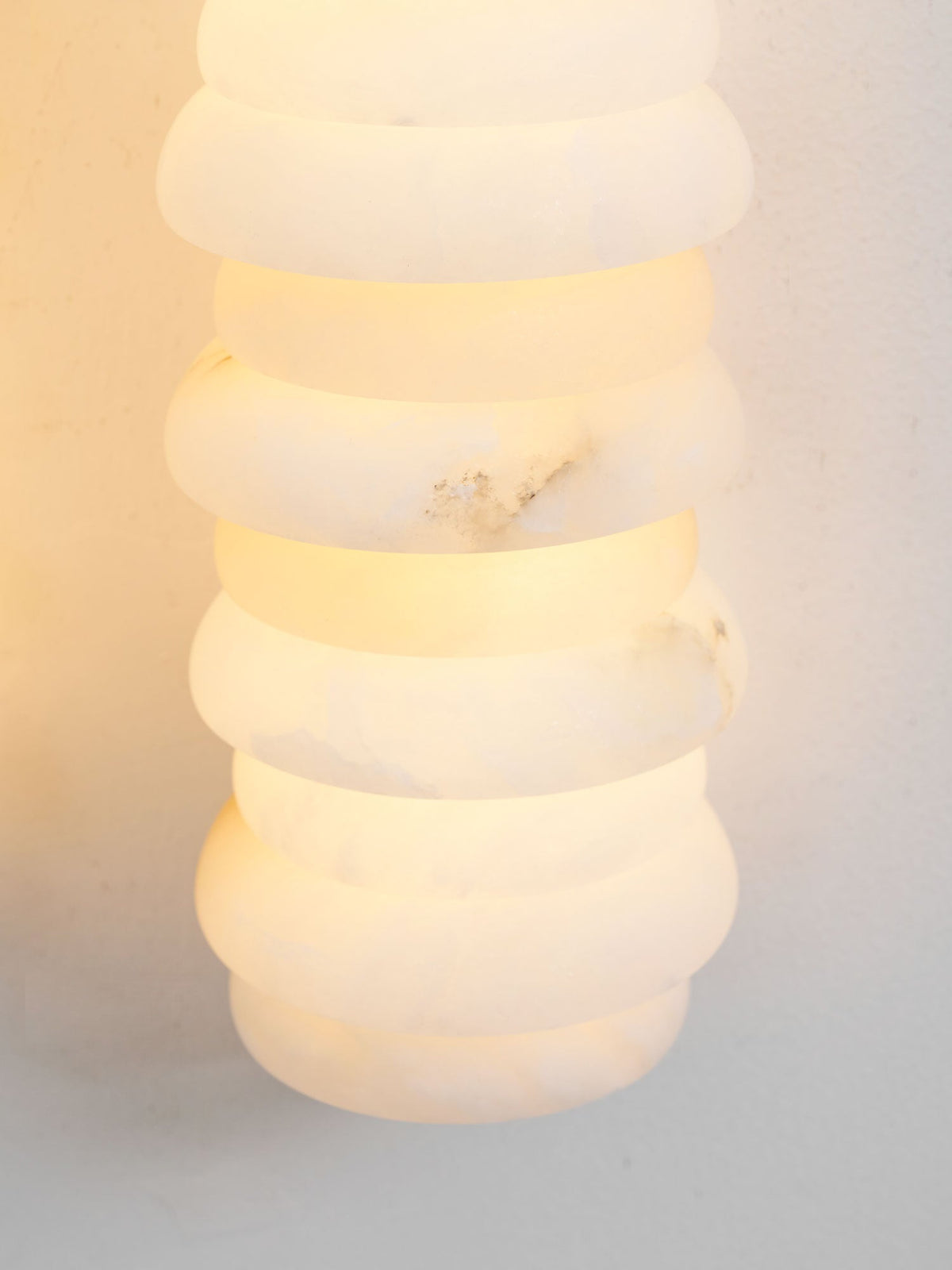 Close view of a lit alabaster column on a Clérachic sconce, the rounded discs glowing with a soft golden-white light.