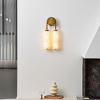 Lit Clérachic sconce in antique brass on a white wall, with a stacked-ceramic vase and a glass on the ledge below.