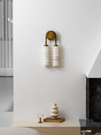 Clérachic antique-brass sconce, unlit, on a tall white wall above a pale ledge with a cream vase and an amber glass.