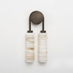 Clérachic sconce in bronze on a white backdrop, with two columns of cream alabaster discs and an arched bronze arm.
