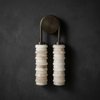 Clérachic sconce in bronze on a dark charcoal plaster wall, the cream alabaster columns standing out against the backdrop.