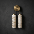 Clérachic sconce in antique brass on a dark charcoal plaster wall, its pale alabaster columns hanging beneath a gold-toned arch.