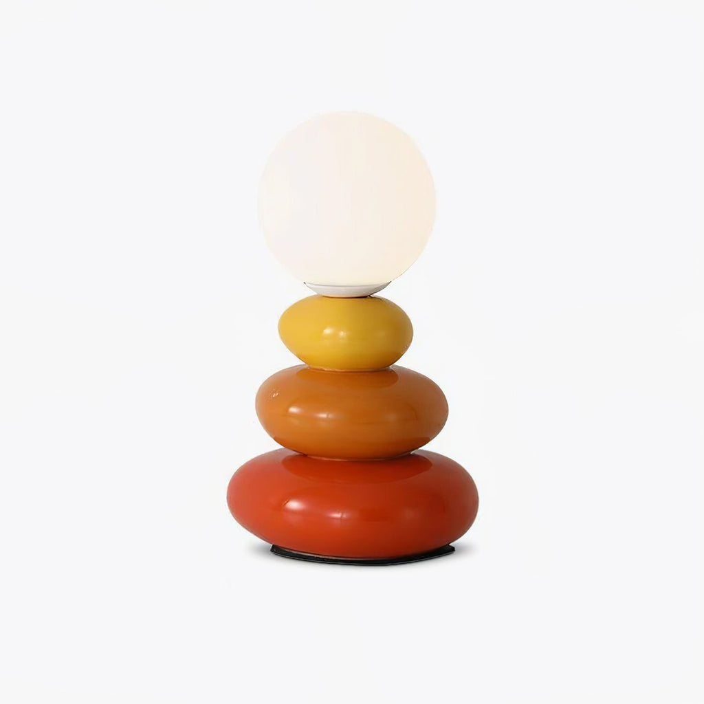 This Clérachic table lamp on a plain white backdrop, a frosted glass globe above three glossy stacked ceramic pebbles in yellow, orange and red.