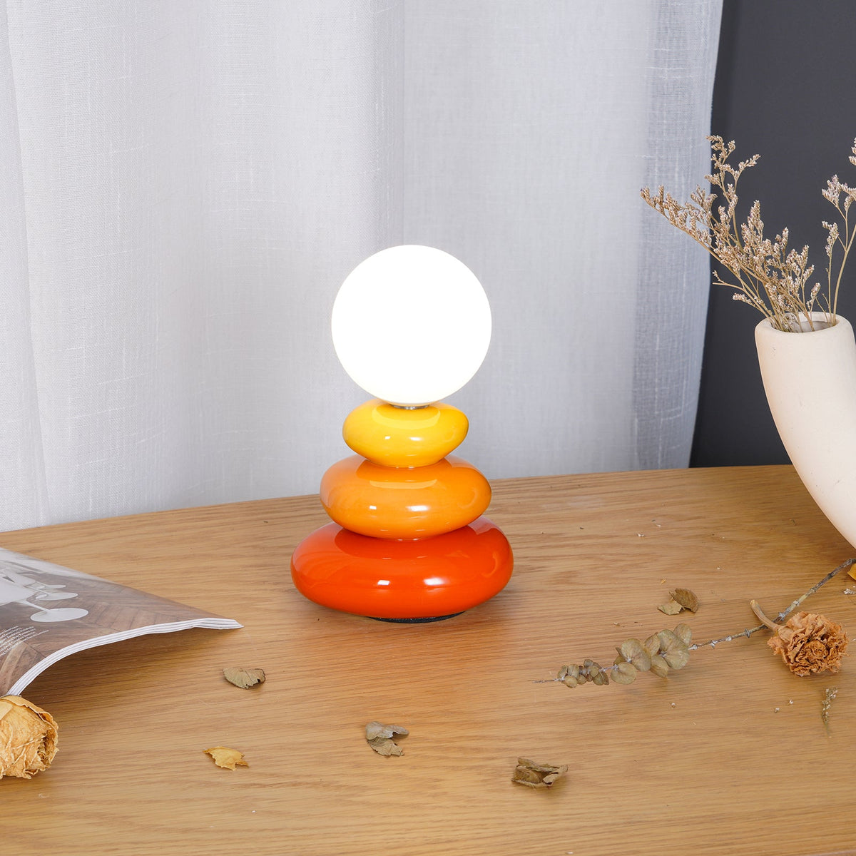 Unlit globe on this Clérachic table lamp, set on a wooden table with a dried-flower vase and a sheer curtain behind.