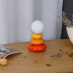Clérachic pebble-stack lamp switched off, its globe a soft grey-white, on a wood table scattered with dried leaves and a folded paper bag.