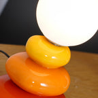 Close view of the glossy yellow and orange ceramic pebbles beneath the glass globe of this Clérachic table lamp.
