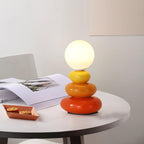 A Clérachic stacked-ceramic lamp glowing on a white round table, beside an open magazine and a small tray of biscuits.