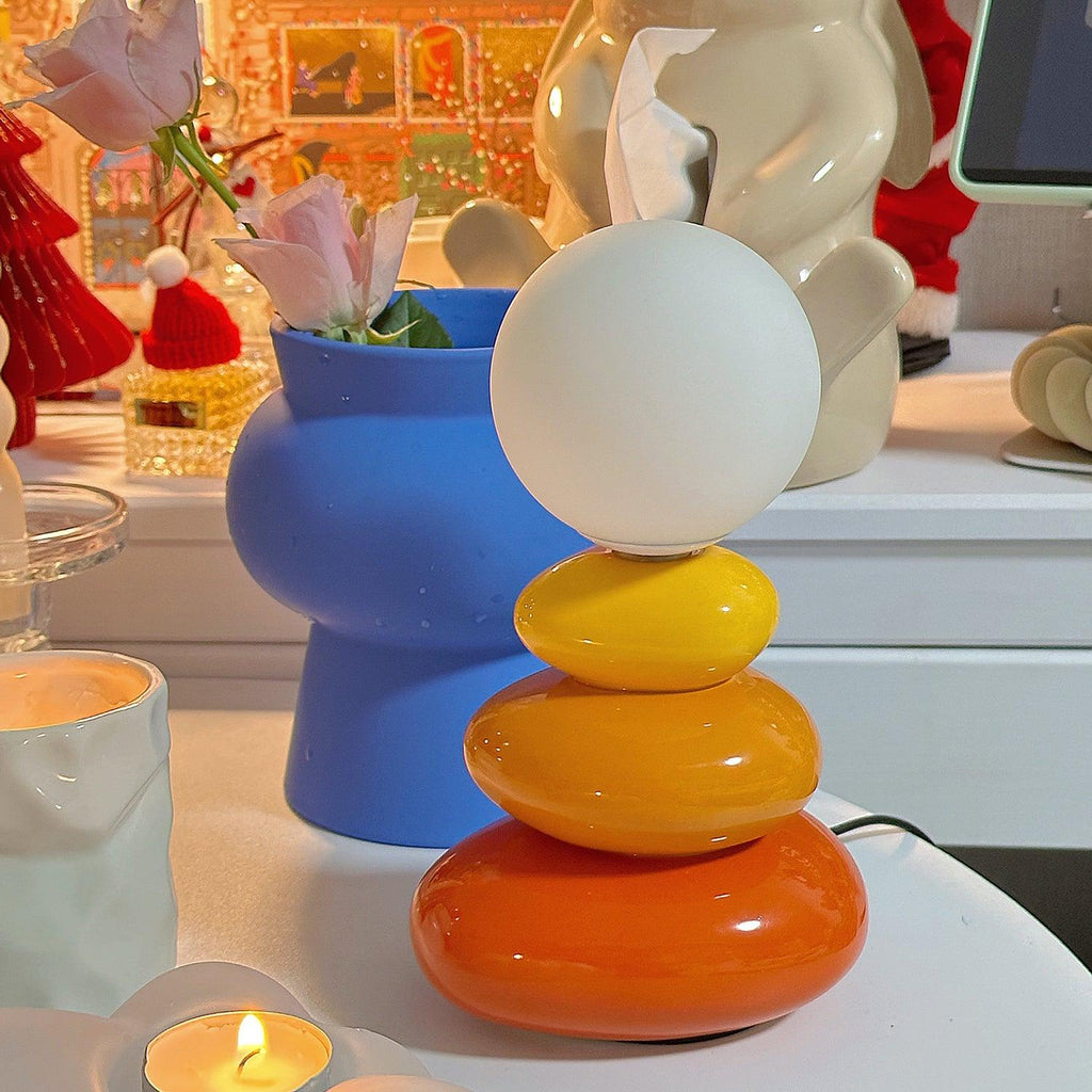 Clérachic table lamp in yellow, orange and red, lit and standing in front of a blue vase on a festive shelf with candles.