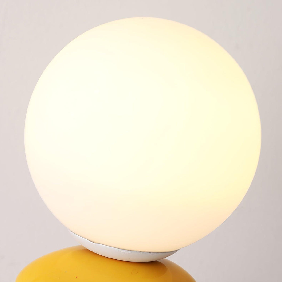 Close view of the frosted glass globe on this Clérachic table lamp, glowing warm white above the yellow top pebble.