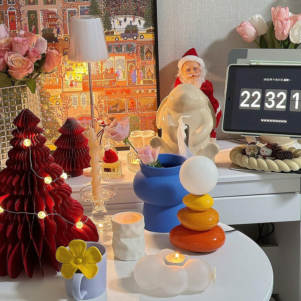 Small Clérachic table lamp in orange tones on a crowded white table, with a blue vase, red paper trees and a Father Christmas figure.