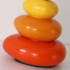 Close view of three glossy ceramic pebbles in yellow, orange and red, the base of this Clérachic table lamp.