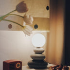 Clérachic table lamp in grey and charcoal tones, lit and glowing behind a spotted fabric lampshade, with a small red radio at the side.