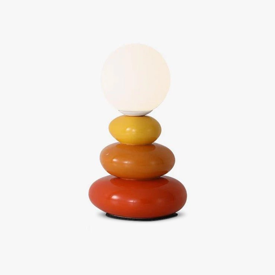 Studio view of this Clérachic table lamp on a plain white backdrop, a frosted globe above yellow, orange and red ceramic pebbles.