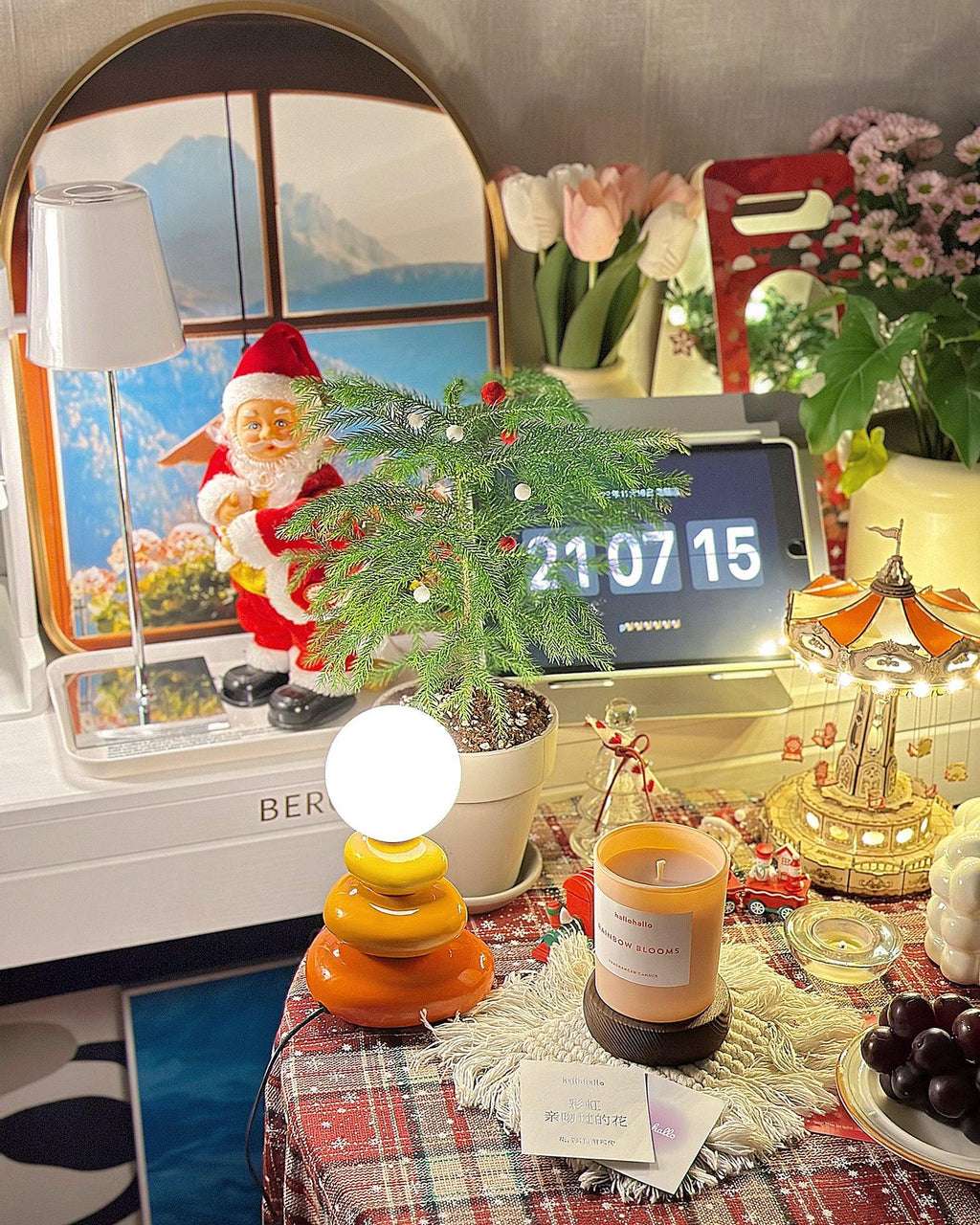 Clérachic table lamp lit on a crowded festive table with a small tree, a candle jar, a clock display and a Father Christmas figure.