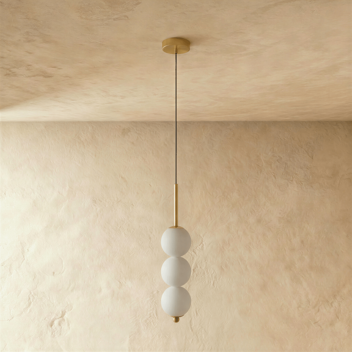 Clérachic gold pendant with three frosted glass spheres on a slim stem, switched off against a warm plaster wall.
