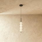 Clérachic black four-ball pendant with glowing opal glass spheres on a slim stem, set against warm limewash.
