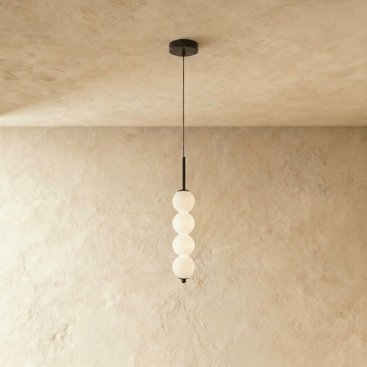Clérachic black four-ball pendant with glowing opal glass spheres on a slim stem, set against warm limewash.