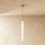 Clérachic eight-ball pendant in gold, a tall column of lit opal glass spheres hanging against a limewash wall.
