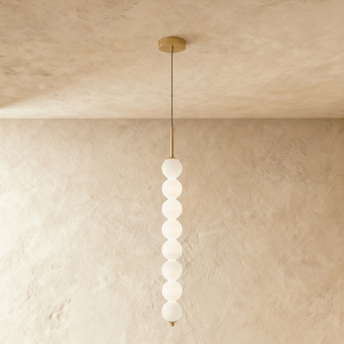 Clérachic eight-ball pendant in gold, a tall column of lit opal glass spheres hanging against a limewash wall.