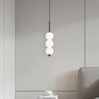 Clérachic black three-ball pendant lit against a grey panelled wall, above a coffee cup and books on a side table.