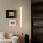 Clérachic gold eight-ball pendant hanging in a living room beside framed art, a cream sofa and a black side table.