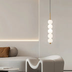 Clérachic gold five-ball pendant glowing in a pale living room with a sculptural white armchair and a cove-lit wall.