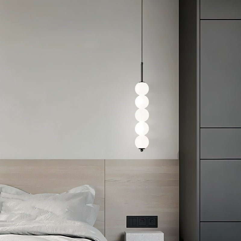 Clérachic black five-ball pendant lit beside a pale oak headboard, with grey wardrobe doors and a wall socket behind.