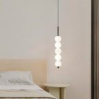 Clérachic black five-ball pendant glowing over a bedside, next to a cream headboard and a round pale side table.