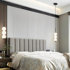 Two Clérachic black three-ball pendants flanking a grey upholstered headboard in a calm bedroom with a panelled wall.