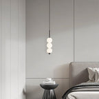 Clérachic black three-ball pendant above a pleated black side table with stacked books, beside a grey upholstered bed.