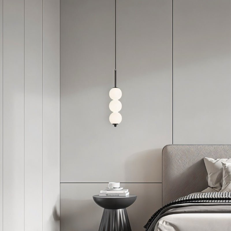 Clérachic black three-ball pendant above a pleated black side table with stacked books, beside a grey upholstered bed.