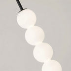 Close detail of a Clérachic black pendant, four glowing frosted glass spheres stacked below a slim black stem.