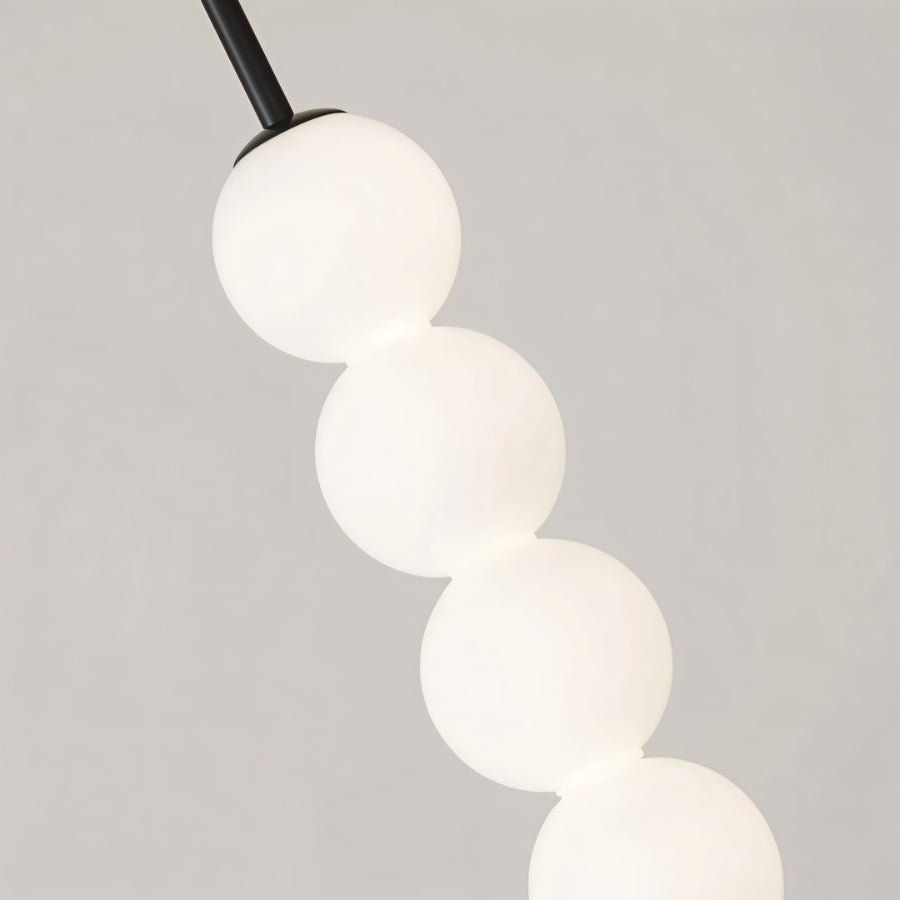 Close detail of a Clérachic black pendant, four glowing frosted glass spheres stacked below a slim black stem.