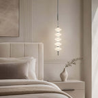 Chrome and white Clérachic pendant of stacked ribbed discs glowing beside an upholstered cream headboard and a bud vase.