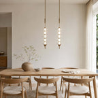 Two gold and clear Clérachic pendants, tall and slim with stacked glass discs, hung above a pale oak dining table.